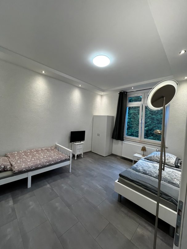 Helles Schlafzimmer mit zwei Betten, Fernseher und Fenster zur Außenansicht.