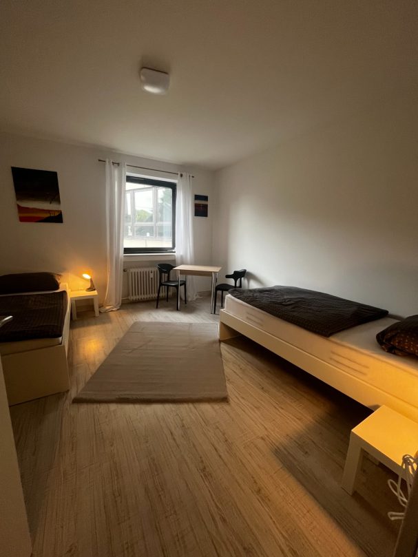 Helles, einfaches Schlafzimmer mit zwei Betten, Tisch und Fenster.